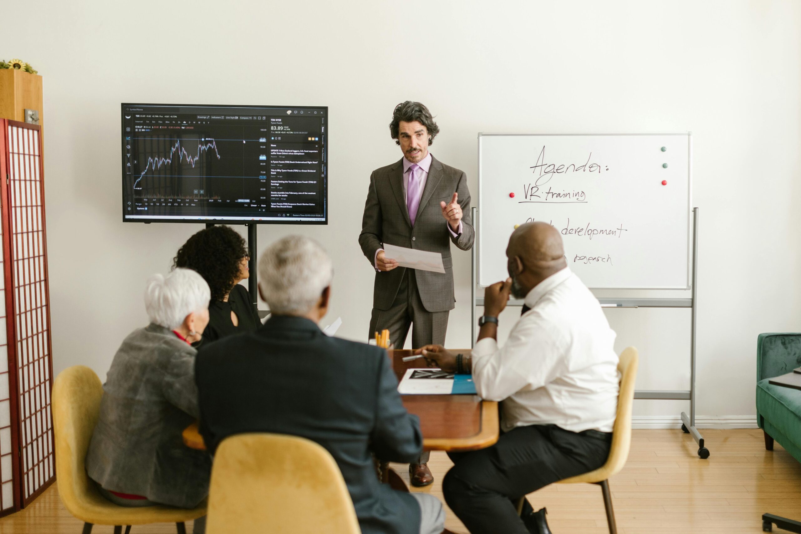 A corporate professional presents market data during a team meeting in an office setting.